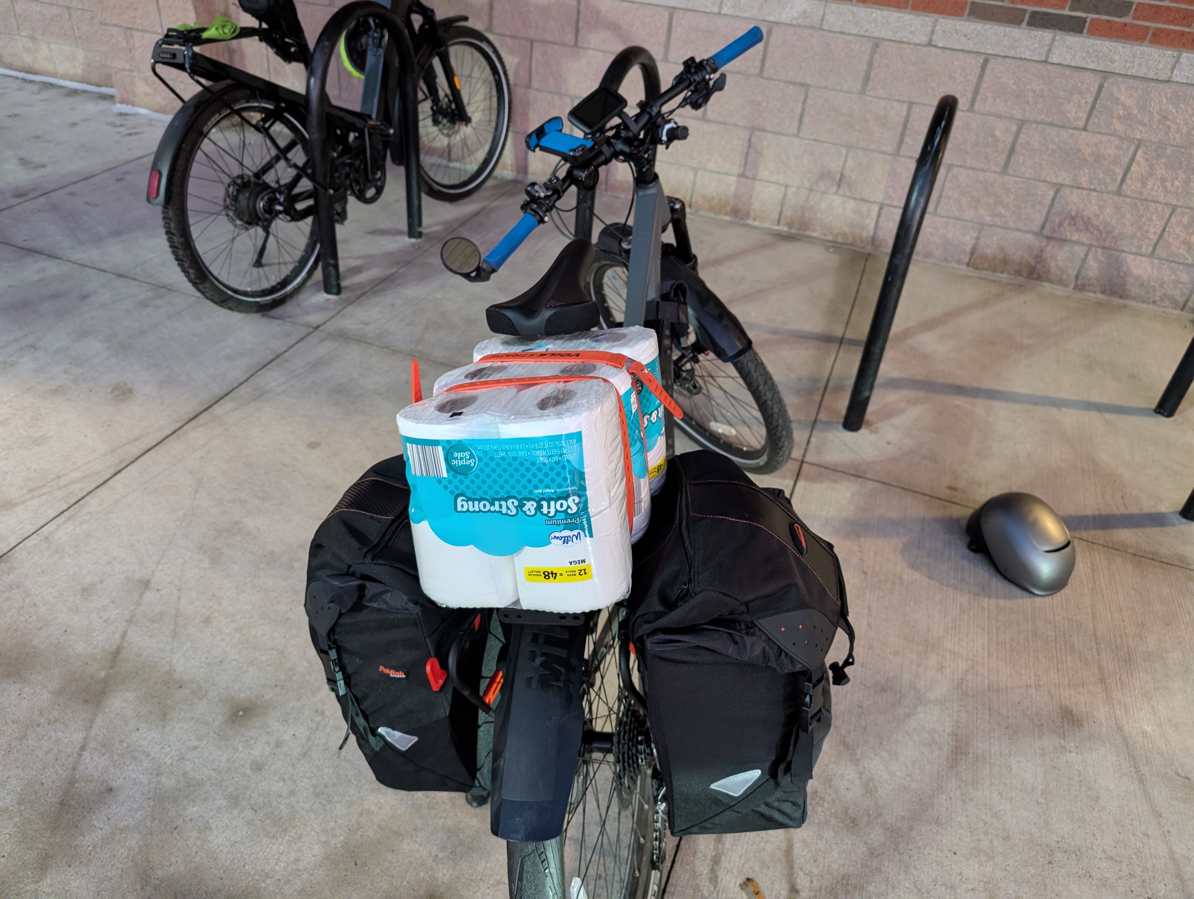 Bicycle at an Aldi bicycle parking, the panniers are full and the rack has a box of toilet paper on top
