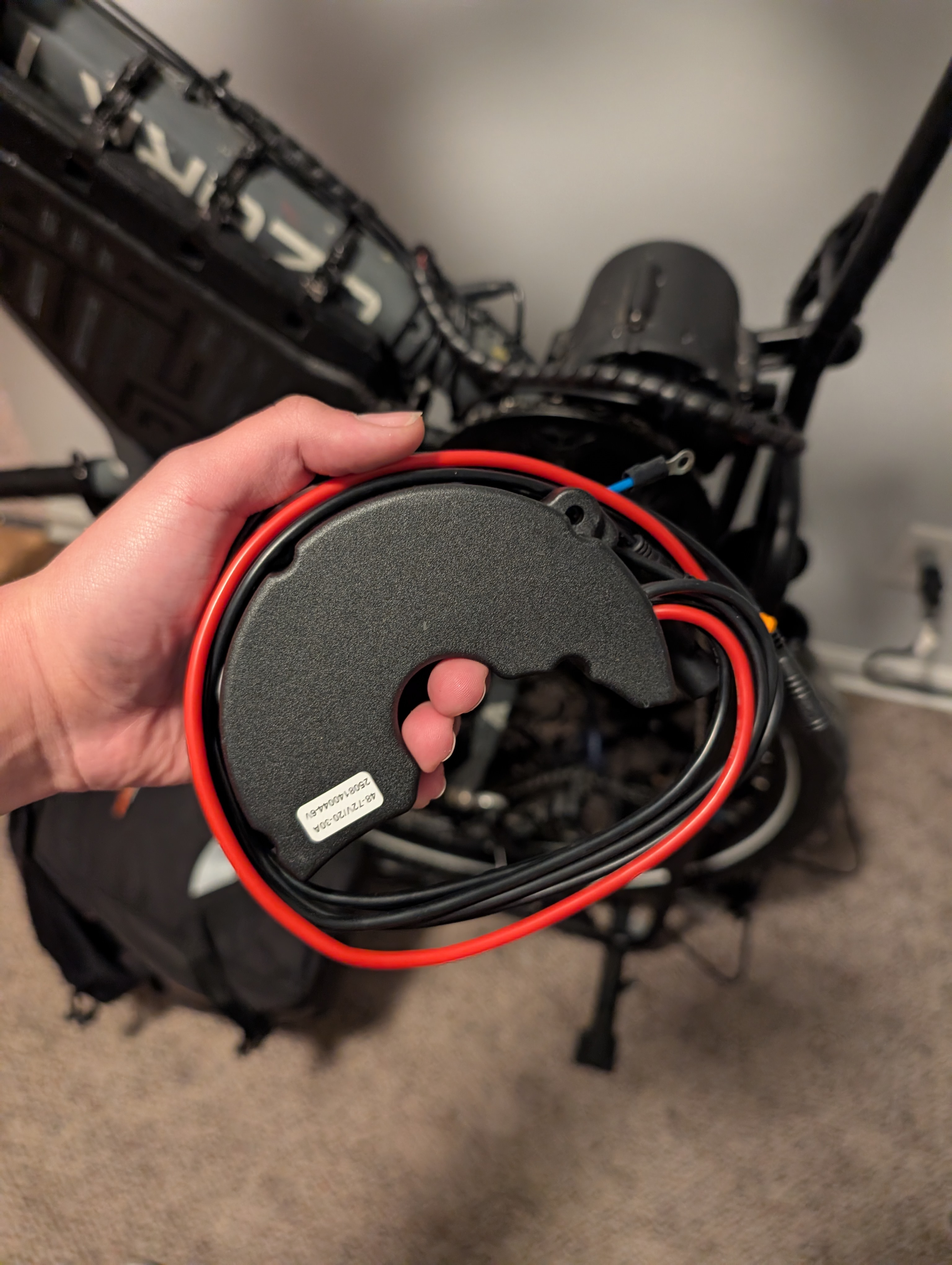 Hand holding the motor controller: a half donut shaped objects with wires outside of it